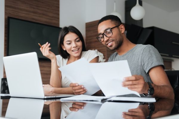 Young couple sitting at their kitchen table with a laptop, looking at their finances.