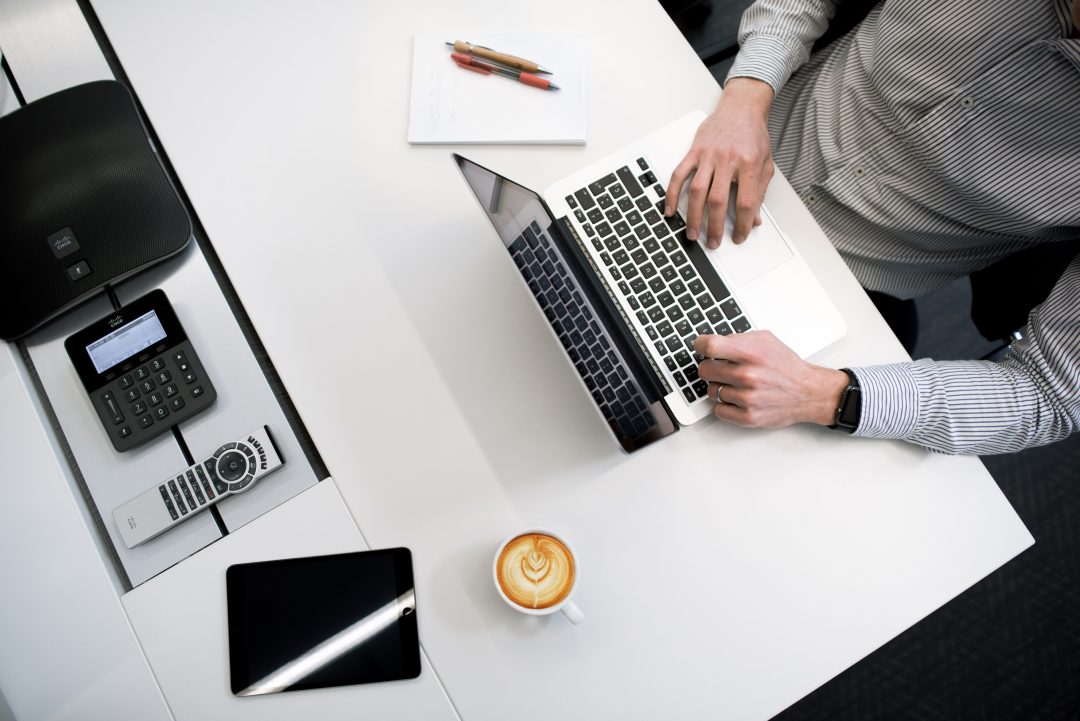 Overhead view of person using a laptop with other digital devices on the desk