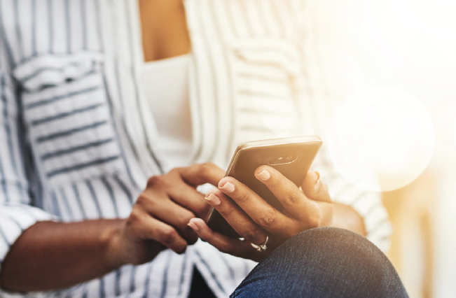 Woman in striped shirt using smartphone with diffused sunlight in the background