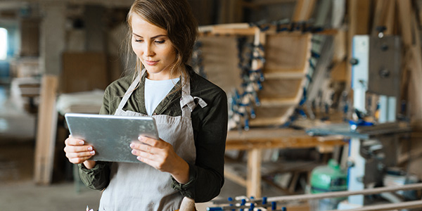 Woman wearing work apron standing in her workshop looking at a tablet