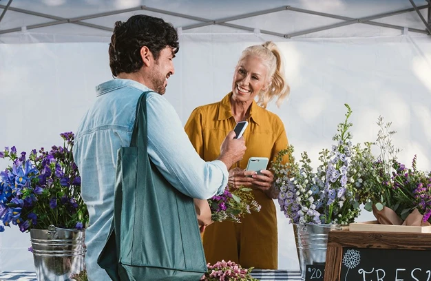 A man purchasing flowers at a florist stand with his smartphone