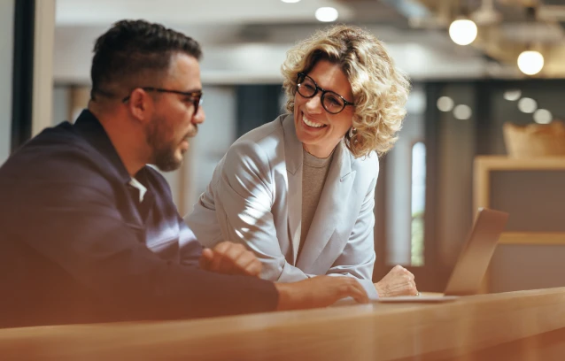 a man and woman talking and smiling while using a laptop computer